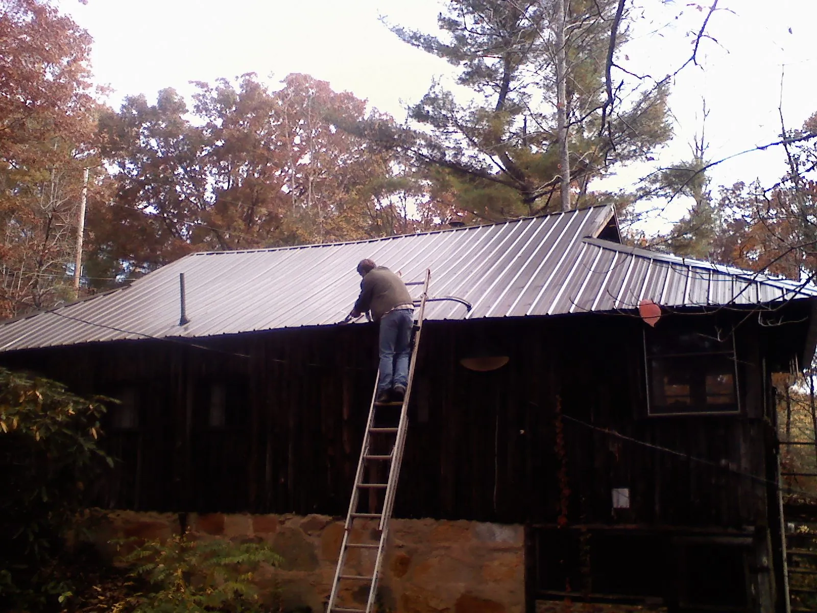 Roofer on a ladder working along the edge of a cabin metal roof in Cloverdale
