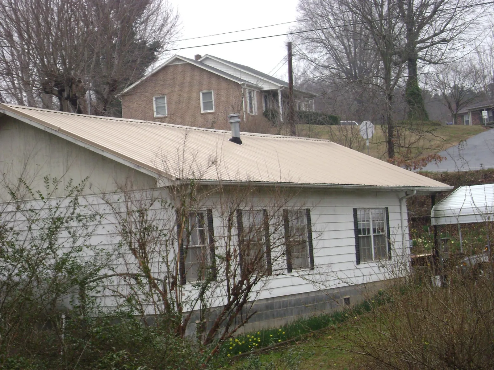 Tan metal roof on a white sided house set into a hillside — Commercial Roofing by Roofing Brothers in Cloverdale